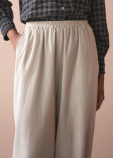 Woman wearing a check shirt and beige corduroy barrel leg trousers against a beige background