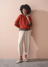 Woman wearing a check shirt and beige corduroy barrel leg trousers against a beige background