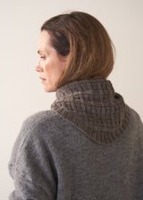 Woman wearing a grey cardigan with a knitted scarf against a plain background