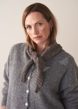 Woman wearing a grey cardigan with a knitted scarf against a plain background