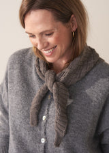 Woman wearing a grey cardigan with a knitted scarf against a plain background