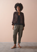 Woman wearing a patterned bubble hem shirt and green trousers against a beige background