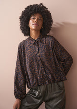 Woman wearing a leopard print bubble hem shirt and khaki trousers against a beige background