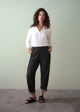 Woman wearing a white blouse and dark jeans against a plain background