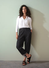 Woman wearing a white shirt and dark jeans against a plain wall.