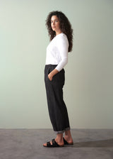 Woman wearing a white top and black jeans against a plain background