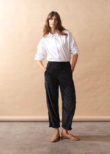 Woman wearing a white shirt and black corduroy trousers against a beige background