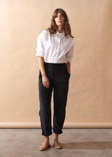 Woman wearing a white shirt and black corduroy trousers against a beige wall