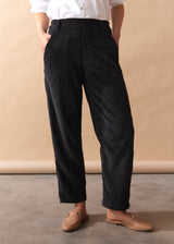 Person wearing black corduroy trousers and beige shoes against a beige background