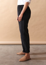 Person wearing black corduroy trousers and brown shoes on a beige background