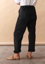 Person wearing black corduroy trousers and a white shirt against a beige background