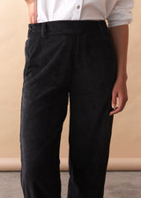 Person wearing black corduroy trousers against a beige background