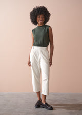 Woman wearing a green sleeveless top and light cream corduroy cropped trousers against a beige background