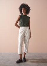 Person wearing a green sleeveless top and light cream corduroy cropped trousers against a beige background