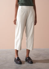 Person wearing light cream corduroy cropped trousers and dark shoes on a neutral background