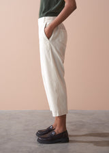 Person wearing light cream corduroy cropped trousers and dark shoes on a plain background