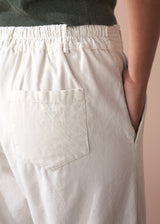 Close-up of a person wearing light cream corduroy cropped trousers with a pocket, on a neutral background.