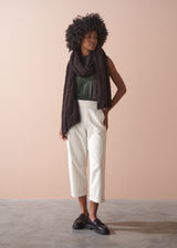 Woman wearing a dark scarf, green top, light cream corduroy cropped trousers, and brown shoes against a beige background