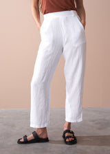 woman wearing a burn orange top with white tapered leg linen trousers and sandals