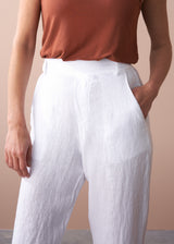 woman wearing a burn orange top with white tapered leg linen trousers