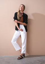 woman wearing a burn orange top and blazer with white tapered leg linen trousers