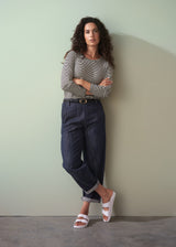 Woman wearing a striped shirt and jeans against a plain wall