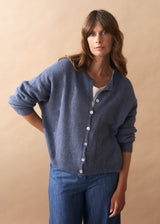 Model wearing light blue wool blend cardigan with mother of pearl buttons and wide leg jeans against a plain background
