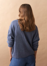 Model wearing light blue wool blend cardigan with mother of pearl buttons and wide leg jeans facing a plain background