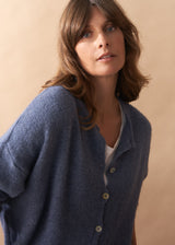 Close up of model wearing in a light blue wool blend cardigan with mother-of-pearl buttons and wide-leg jeans.