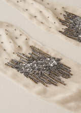 Close-up of a cream-colored sheer tights or stockings featuring intricate silver and gold beaded embellishments and sequins.