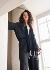 Woman wearing a black sheer shirt, wide leg trousers and velvet scarf