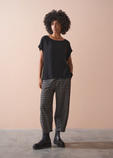 Person wearing a black top and checkered barrel leg trousers against a beige background