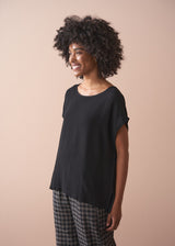 Woman wearing a black top and plaid barrel leg trousers against a beige background