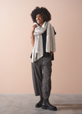 Woman wearing a patterned scarf, black top, plaid barrel leg trousers, and black boots against a beige background