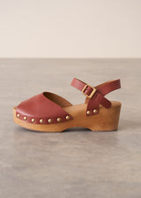 Brown wooden clog shoe with a strap on a neutral background