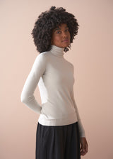 Woman wearing a white turtleneck sweater against a beige background