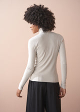 Person wearing a white turtleneck sweater and black pants against a beige background