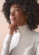 Woman wearing a white turtleneck sweater against a beige background
