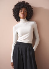 Woman wearing a white turtleneck and black pants against a beige wall