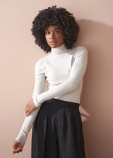 Woman wearing a white turtleneck and black skirt against a beige wall