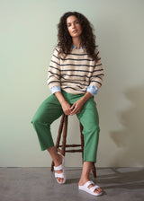 Woman sitting on a stool wearing a striped sweater and green cotton tapered trousers against a plain background