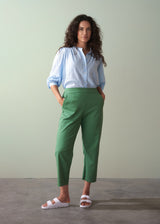 Woman wearing a light blue shirt and green cotton tapered trousers against a plain background