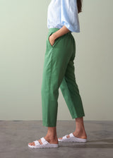 Person wearing green cotton tapered trousers and white sandals on a plain background