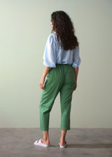 Woman wearing a light blue shirt and green cotton tapered trousers against a plain background