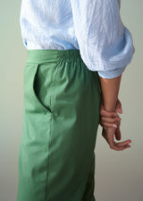 Person wearing a white shirt and green cotton tapered trousers against a plain background