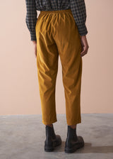 Woman wearing a black checked shirt and mustard corduroy trousers against a beige background