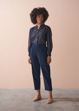 Woman wearing a navy shirt and navy corduroy trousers against a beige background