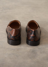 A pair of men's slip-on loafers with a brown and black snakeskin pattern, shown from the back on a textured gray concrete surface.