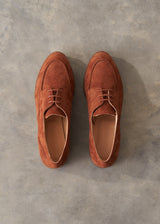 A pair of brown suede derby shoes shown from a top-down view on a textured gray concrete surface.