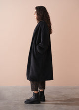 Person wearing a black coat standing against a beige background